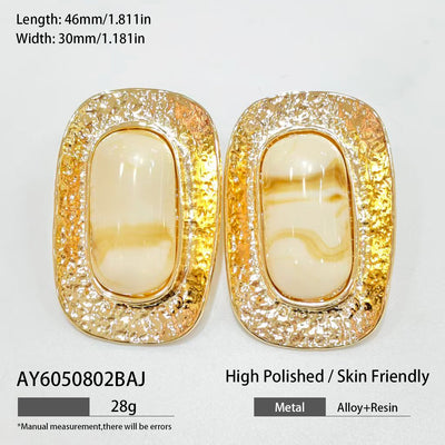 Flat lay of 18K gold plated marbled resin oval stud earrings on neutral background.
